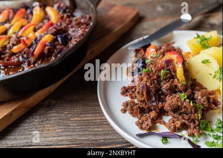 Rindereintopf mit Rotkohl und gekochten Äpfeln und Kartoffeln auf einem Holztisch Stockfoto