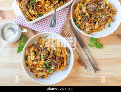 Geschmortes Rindfleisch mit Pasta und Parmesankäse auf Tellern auf einem Kiefernholztisch. Flach verlegt Stockfoto