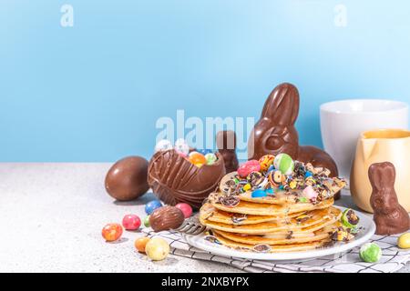 Kinder haben ein lustiges, süßes Osterfrühstück. Amerikanische Pfannkuchen, gebratene Teigkuchen mit Osterschokoladeneiern, Marshmallows, Zuckergarn mit gebrochenen Stockfoto