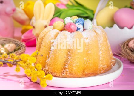 Traditioneller Osterkuchen. Süßes, traditionelles Ostergebäck mit Zuckerpulver, bunten Ostereiern, Frühlingsblumen, rosa gelb Stockfoto