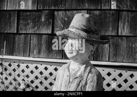 Eine alte verwitterte Statue eines Jungen, der am Meer entlang des Spazierwegs am North Hampton Beach, New Hampshire, sitzt. Das Bild wurde analog aufgenommen Stockfoto