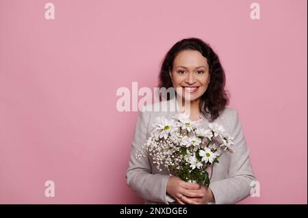 Attraktive Frau mittleren Alters mit einem süßen Strauß Chrysanthemen Blumen, lächelnd vor die Kamera, isolierter rosa Hintergrund Stockfoto