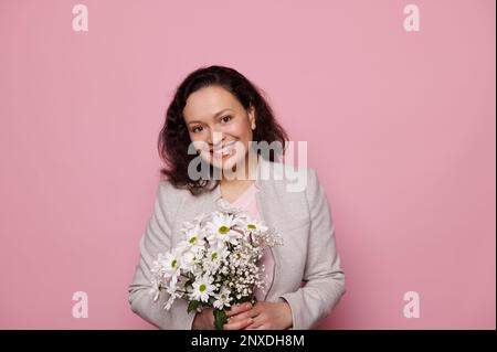 Hübsche Frau mittleren Alters, die sich glücklich fühlt, während sie einen süßen Blumenstrauß für den Internationalen Frauentag bekommt. Werbefläche Stockfoto