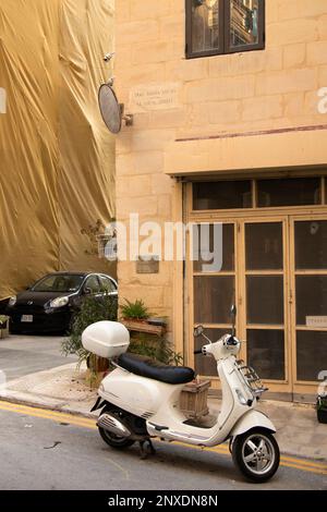 Valletta, Malta - 11. November 2022: Weißer vespa Vintage Roller parkt vor dem KalksteinEckhaus Stockfoto