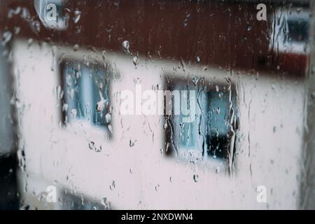 Regentropfen auf einer transparenten Oberfläche aus Fensterglas. Fällt an regnerischen Tagen auf den Fensterschild. Stürmisches Wetter. Isolation, trauriges Depressionskonzept. Regnerische Stockfoto