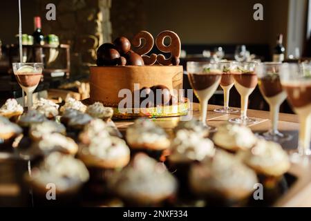 Schokoriegel. Köstliches süßes Buffet mit braunem Geburtstagskuchen dekorierte Schokoladenbällchen und Nummer 29, Cupcakes mit weißer Milchcreme, Mousse Desserts. Stockfoto