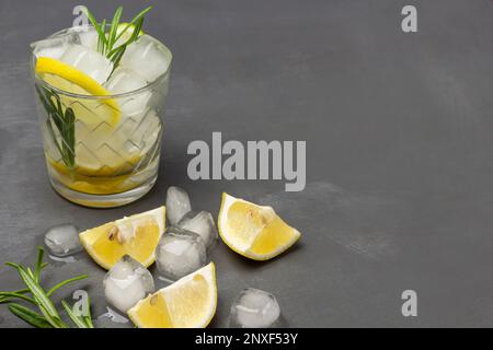 Zitronen-Kühlgetränk mit Rosmarin. Zitronen und Eis auf dem Tisch. Speicherplatz kopieren. Draufsicht. Grauer Hintergrund. Stockfoto