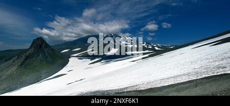 Vulkankankegel anstelle des Fissurenausbruchs. Ein großer erloschener Vulkan, bedeckt mit Wolken am Horizont. Die Leute auf dem Schneefeld geben einen Hinweis auf den sc Stockfoto