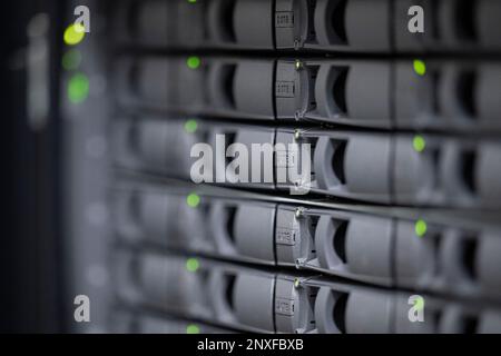 Schärfentiefe der grauen Festplattensteckplätze eines an das IT-Netzwerk angeschlossenen Speichergeräts mit grünen LEDs Stockfoto