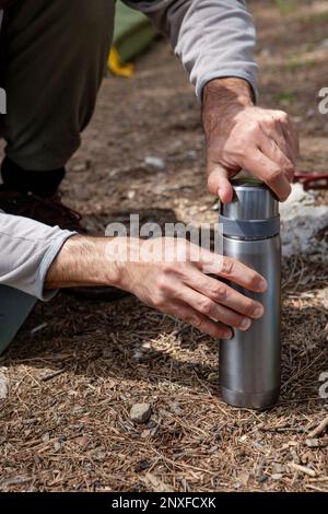 Der Mann stellt Thermosflaschen auf einen Baumstumpf Stockfoto