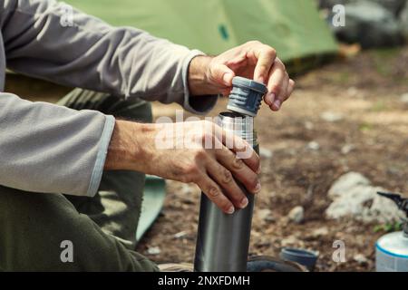 Der Mann stellt Thermosflaschen auf einen Baumstumpf Stockfoto