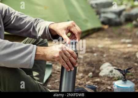 Der Mann stellt Thermosflaschen auf einen Baumstumpf Stockfoto