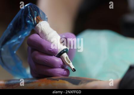 Tattoo-Meister, der mit der Drehmaschine arbeitet. Professioneller Tätowierer trägt sterile Handschuhe und verwendet eine moderne Pistole, um Tintenkunst auf der Haut zu kreieren Stockfoto