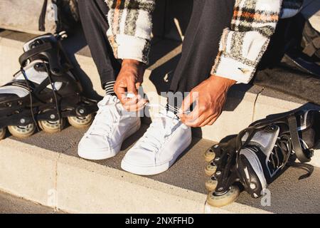 Nahaufnahme von Männerfüßen beim Vorbereiten der Inline-Skates. Ein Mann, der sich fürs Skaten vorbereitet Stockfoto