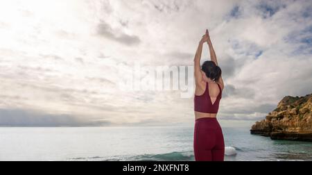 Eine Frau, die am Meer steht, mit erhobenen Armen meditiert, ein Konzept der Kopfräume. Stockfoto