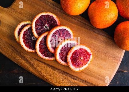 Blut-Orange-Scheiben auf einem Holzbrett: Geschnittene Zitrusfrüchte mit Vollblutorangen an der Seite Stockfoto