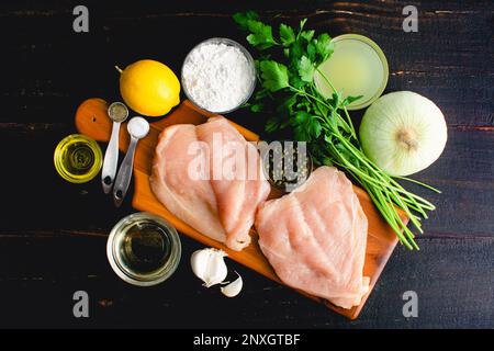 Gesundes Huhn Piccata Inhaltsstoffe auf einem Holztisch: Aufgehellte Chicken Piccata Zutaten auf dunklem Hintergrund Stockfoto