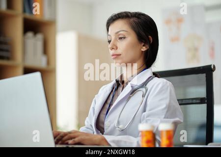 Der Arzt füllt das Formular auf dem Laptop aus, wenn er ein Rezept für den Patienten ausstellt Stockfoto