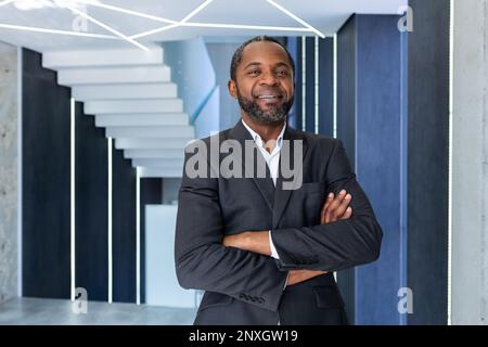 Porträt des erfolgreichen afroamerikanischen Chefs, Geschäftsmann im Business-Anzug, der lächelt und mit gekreuzten Armen in die Kamera schaut, Mann zufrieden mit Arbeit und Leistungen. Stockfoto