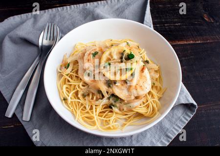Hähnchen Piccata über Spaghetti in einer Pastaschale: Hähnchen, Zwiebeln und Zitronen in Sauce aus Knoblauch und Weißwein Stockfoto