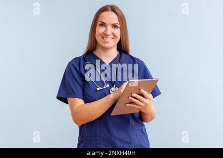 Lächelnde junge Ärztin arbeitet auf einem Tablet auf blauem Hintergrund Stockfoto