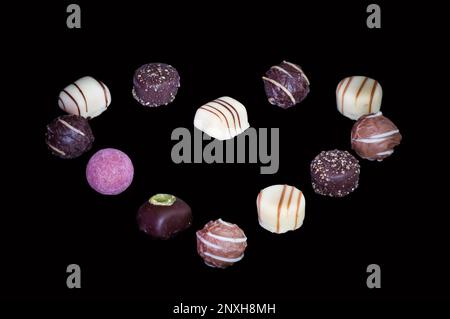 Verschiedene Pralinen von Schokoladentrüffeln, isoliert auf schwarzem Hintergrund. In Herzform angeordnet. Stockfoto