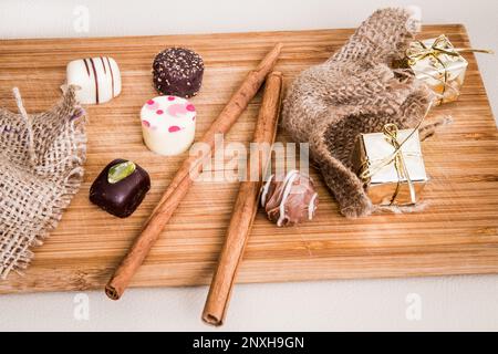 Schokoladen-Mini-Pralinen, dekoriert mit Zimtstäbchen und kleinen Packungen in Goldfarben, auf dem Tisch angeordnet. Stockfoto