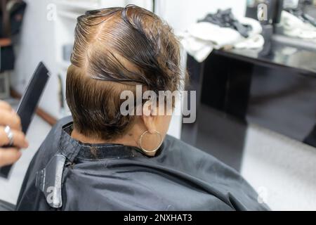 Rückansicht von nassem Haar mit einer Linie in der Mitte des Kopfes auf einem verschwommenen Hintergrund, Stylist schneidet einer älteren Frau die Haare, braune Farbe, Schönheitssalon Verfahren Stockfoto
