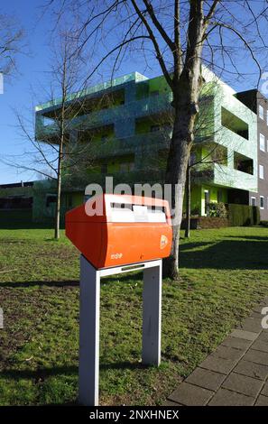 Beekbergen, Niederlande - Februar 28 2023 ein orangefarbener Briefkasten vor einem modernen grünen Apartmentgebäude im Herzen des Dorfes Beekbergen. Stockfoto