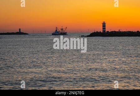 Fischerboot in Silhouette kurz nach Sonnenuntergang zwischen zwei Leuchttürmen am südlichen und nördlichen Pier Ijmuiden, Niederlande Stockfoto