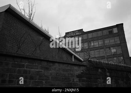 Bolton Textile Mill (Cawdor Street, Farnworth). Ein großes Ziegelgebäude und eine Wand mit Stacheldraht stehen vor dem Betrachter. England, Großbritannien Stockfoto