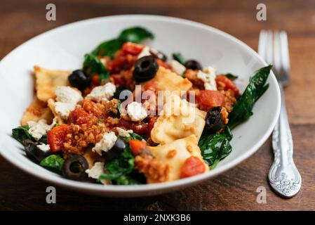 Schüssel mit veganen Ravioli mit Spinat, TVP, Oliven, Tomatensauce und hausgemachten veganen Feta. Stockfoto