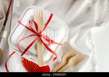 Eine geschlossene Bento-Kuchenbox mit einem Holzlöffel und einem roten Band. Geschenkbox mit leckerem Bento. Kuchenverpackung. Lieferung. Selbstgebackene Idee für den Urlaub. Klein b Stockfoto