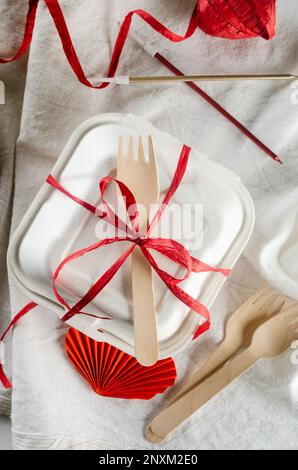 Eine geschlossene Bento-Kuchenbox mit einem Holzlöffel und einem roten Band. Geschenkbox mit leckerem Bento. Kuchenverpackung. Lieferung. Selbstgebackene Idee für den Urlaub. Klein b Stockfoto