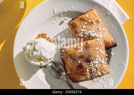Maltesisches Gebäck mit Dattelfüllung namens Imqaret serviert mit Eiscreme auf dem Teller. Stockfoto