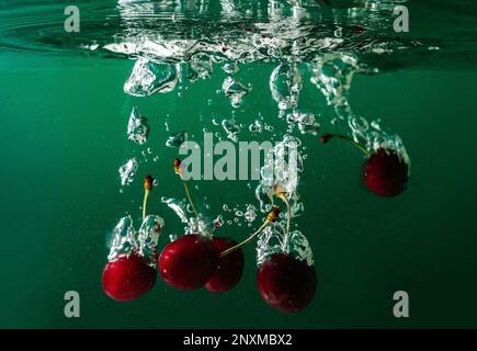 Reife Kirschen fallen ins Wasser und verursachen Spritzer und Luftblasen Stockfoto