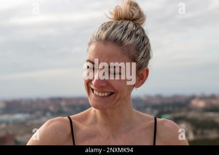 Porträt einer blonden, hübschen, reifen Frau mit grünen Augen in einem schwarzen T-Shirt und Haarschnitt mit Schleife im Hintergrund der Stadt Madrid Stockfoto