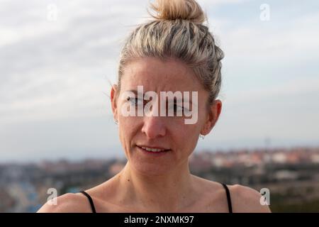 Porträt einer blonden, hübschen, reifen Frau mit grünen Augen in einem schwarzen T-Shirt und Haarschnitt mit Schleife im Hintergrund der Stadt Madrid Stockfoto