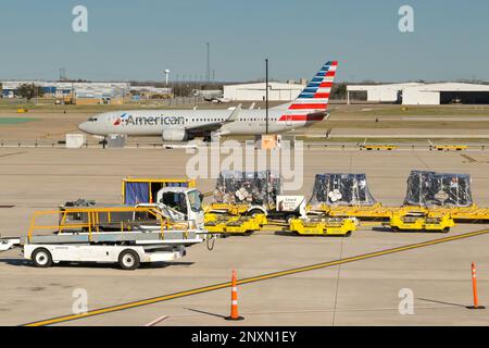 Austin, Texas - Februar 2023: Gepäckladegeräte und Luftfrachtpaletten am Stadtflughafen. Eine American Airlines Boeing 737 fährt Rollen Stockfoto