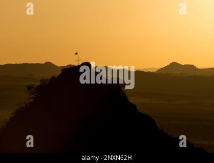 Abenddämmerung mit Blick auf einen kleinen Berggipfel mit Kreuz und Flagge oben. pico dos pireneus - Goiás - Brasilien. Stockfoto