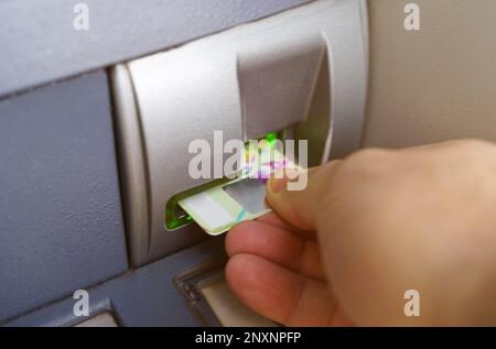 Die Hand einer Person mit einer Kreditkarte an einem Geldautomaten. Nahaufnahme. Stockfoto