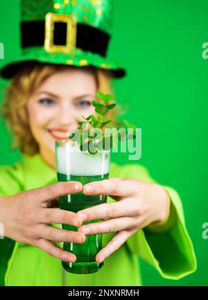 Tag Der Patricks. Grünes Bier mit Klee. Eine Frau mit Koboldhut, die eine Tasse grünes Bier in der Hand hält. Patrick Day Pub-Party feiert. Irische Tradition Stockfoto