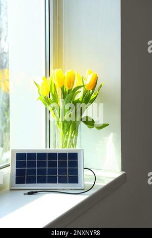 Tragbare Solarpaneele und Vase mit Tulpen auf Fensterbank im Zimmer Stockfoto