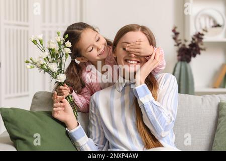 Ein kleines Mädchen mit Blumen, das zu Hause die Augen seiner Mutter schließt Stockfoto