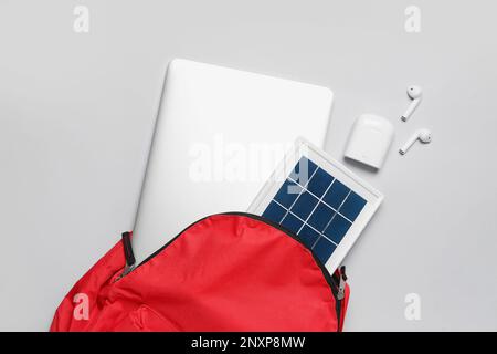 Tasche mit tragbarem Solarpanel, Laptop und Ohrhörern auf hellem Hintergrund Stockfoto