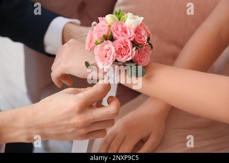 Teenager-Junge, der Ansteckblume um das Handgelenk seiner Freundin bindet, für den Abschlussball im Zimmer, Nahaufnahme Stockfoto