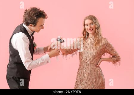 Ein junger Mann, der das Handgelenk seines Abschlussball-Dates auf pinkfarbenem Hintergrund umbindet Stockfoto