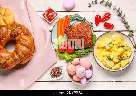 Leckere Gerichte und bemalte Eier zum Osterdinner auf hellem Holzhintergrund Stockfoto