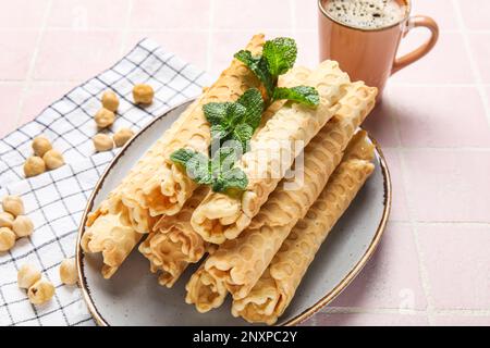 Teller mit köstlichen Waffeln, Minze, Haselnüssen und einer Tasse Kaffee auf pinkfarbenem Fliesenhintergrund Stockfoto