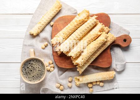 Gehen Sie an Bord mit köstlichen Waffeln, einer Tasse Kaffee und Haselnüssen auf weißem Holzhintergrund Stockfoto